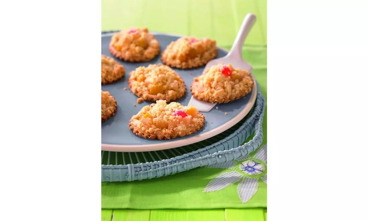 Bănuți crocanți cu martipan și topping de cocktail de fructe viu colorat, așezați pe o farfurie albastră înconjurată de un suport rustic verde
