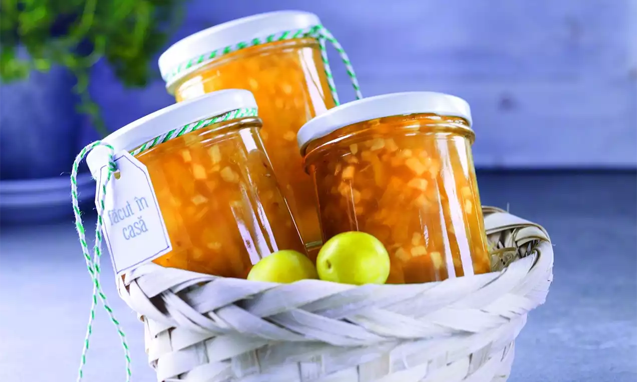 Borcan de dulceață cu bucăți aurii de mere și zarzare, în sirop translucid, aranjate într-un coș alb alături de fructe galbene