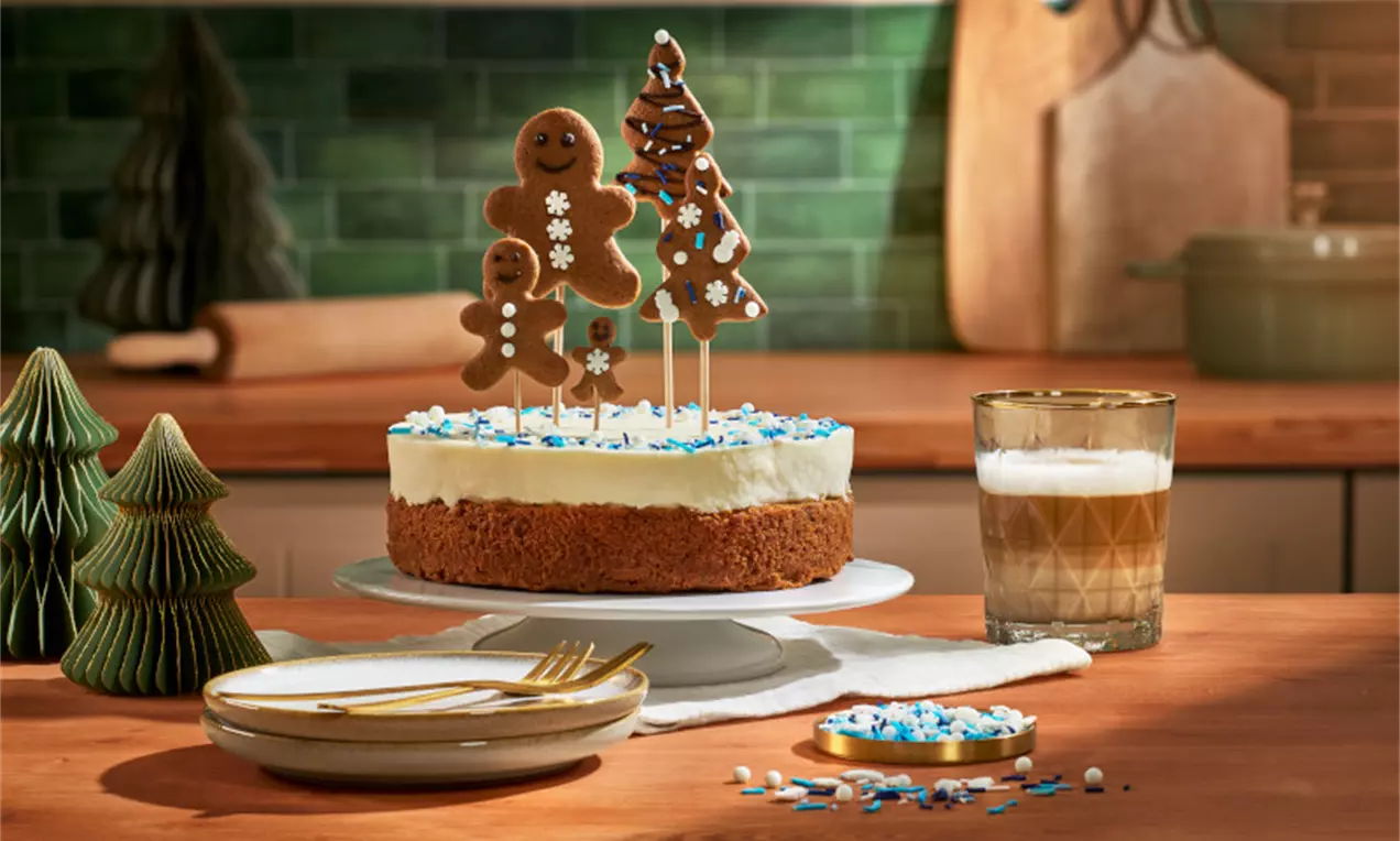 Tort cu blat auriu, strat cremos alb, decorat cu figurine din turtă dulce și ornamente albastre și albe, pe un suport rotund elegant