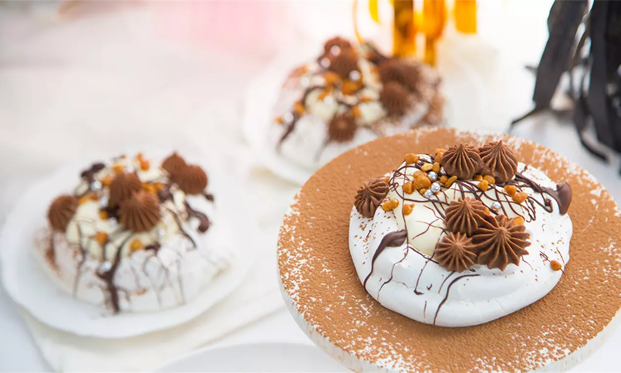 Bezele alb strălucitor cu cremă maronie, decorate cu ciocolată topită, caramel și mici sprâncene aurii pe farfurii pudrate cu cacao