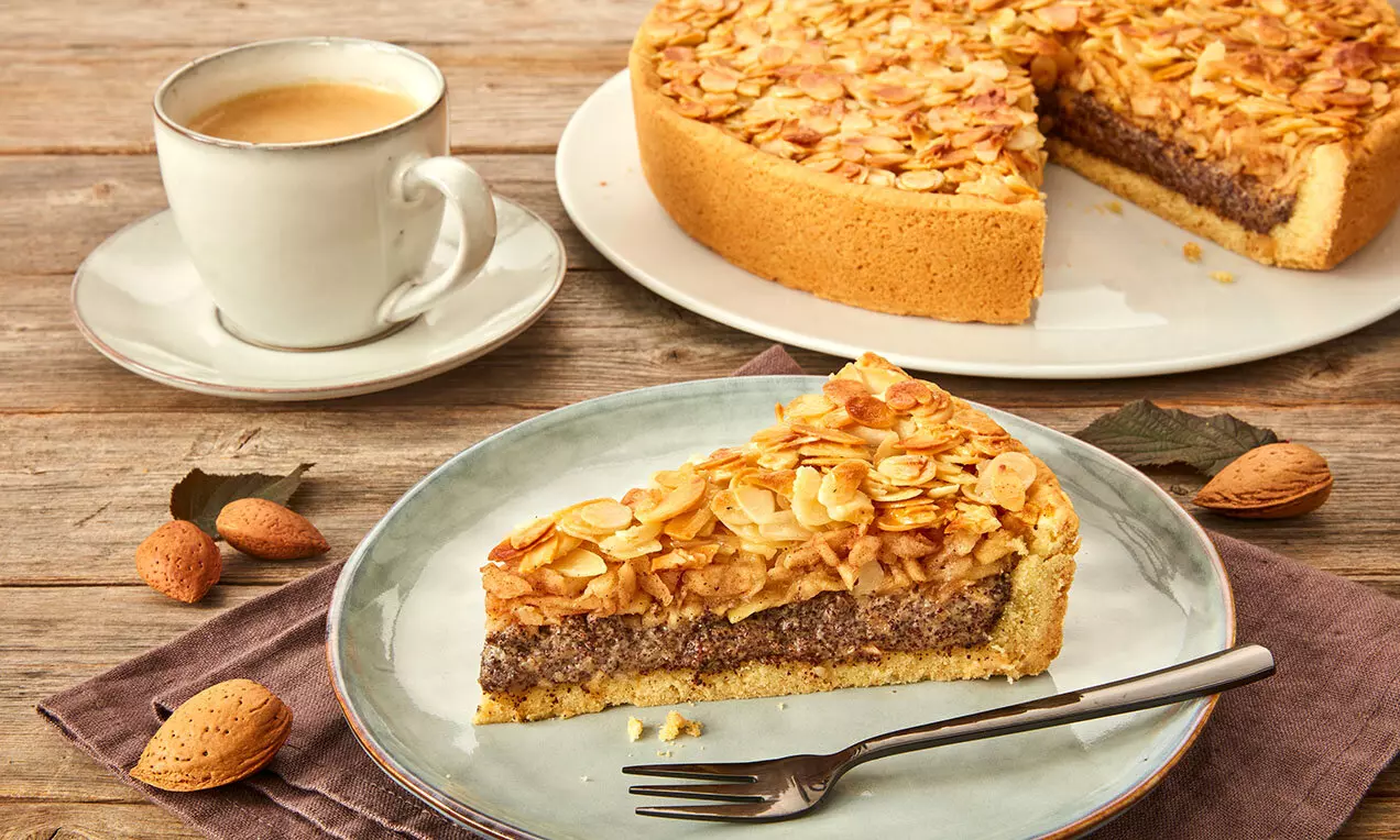 Plăcintă aurie cu mere suculente și strat generos de mac, decorată cu fulgi crocanți de migdale pe farfurie ceramică lângă o ceașcă de cafea