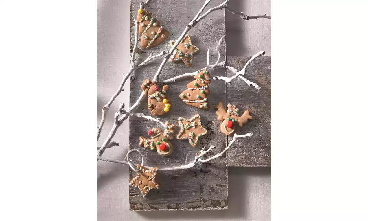 Fursecuri maronii cu scorțișoară în diverse forme festive, decorate cu glazură colorată și sprinkles, așezate pe crengi albe și lemn gri