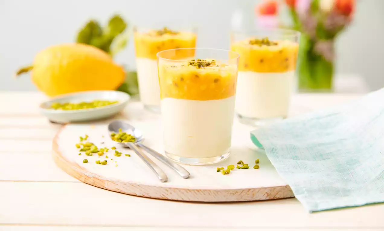 Mousse cremos galben-pal de iaurt cu lămâie în pahare transparente, acoperit cu sos de mango-portocaliu și fistic tocat pe deasupra