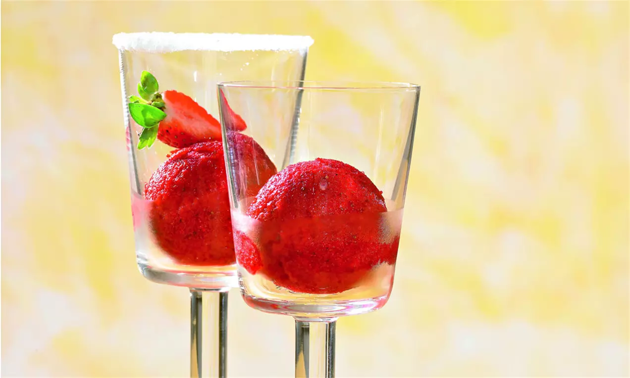 Bile de sorbet din căpșuni roșii intens, cu textură fină, așezate în pahare transparente decorate cu frunze de mentă și felii de căpșuni